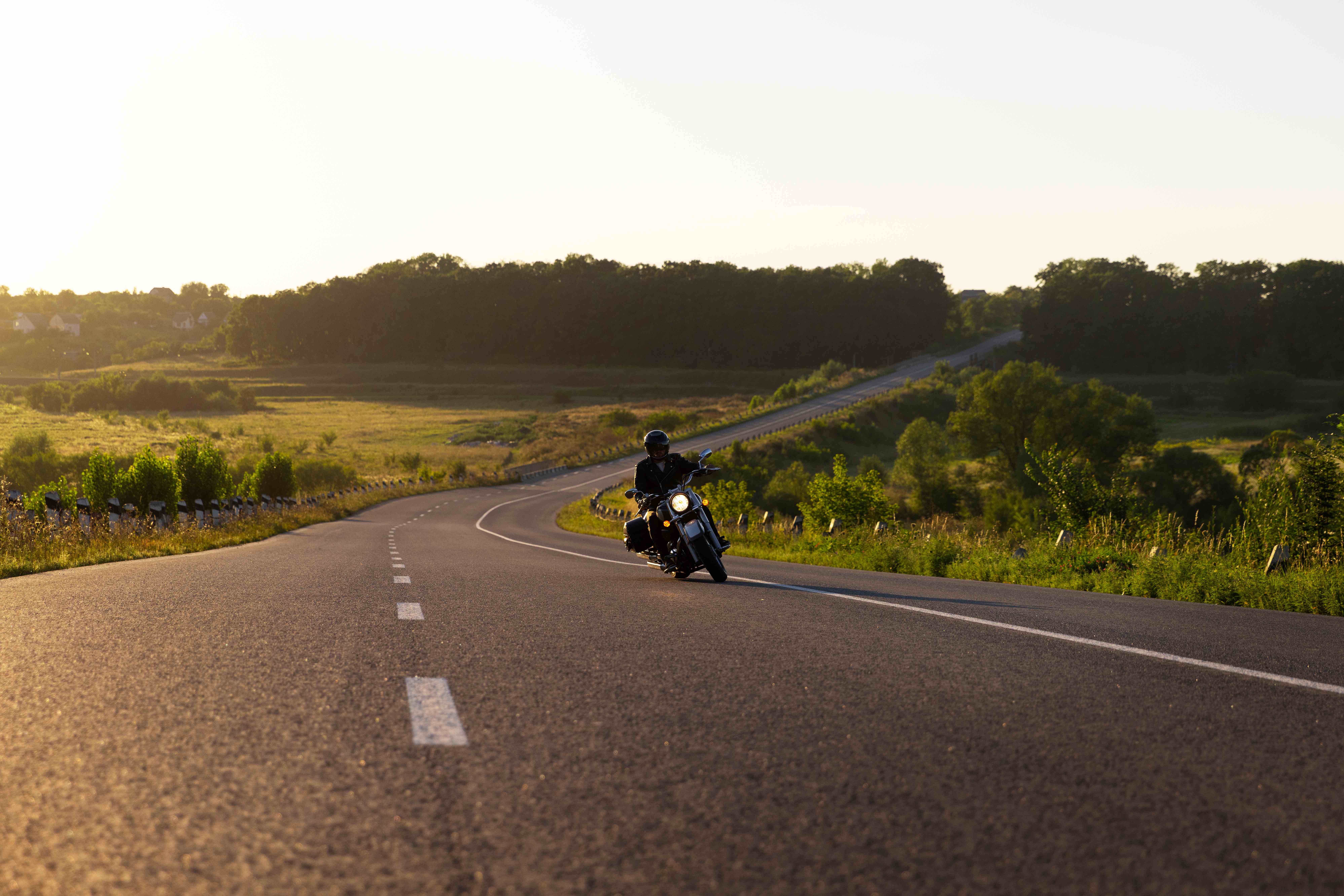 Motorcyclist riding on a winding country road at sunset